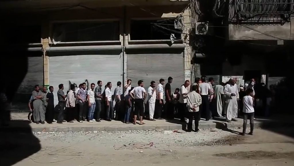 سوريون ينتظرون للحصول على الخبز في مدينة حلب عام 2012 – صورة أرشيفية من صوت أميركا